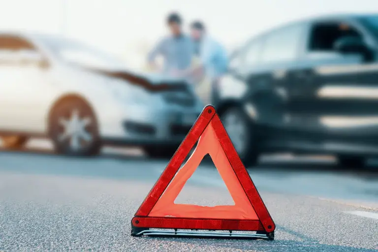 warning road sign on a road with two clashed cars behind