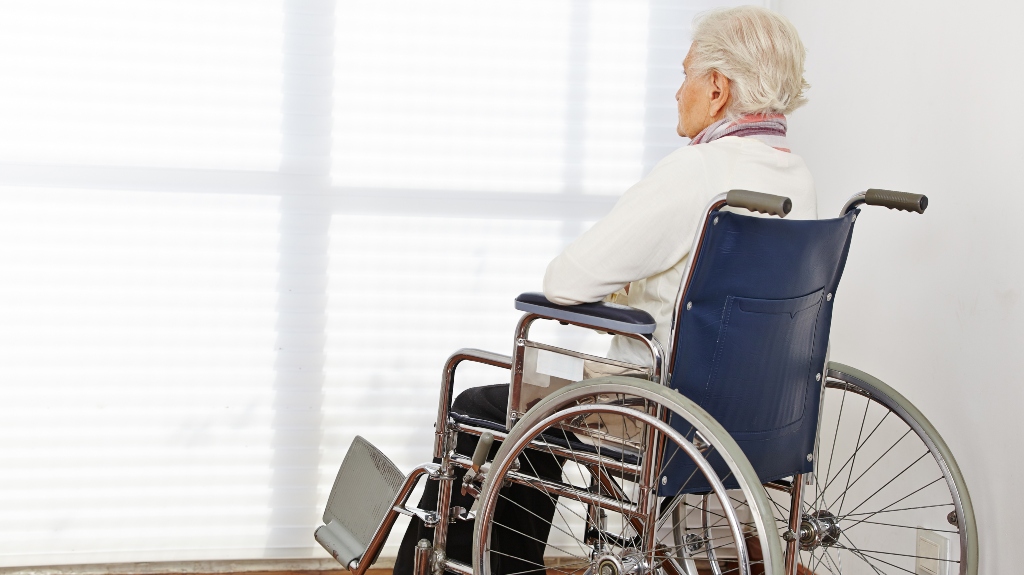 sad senior woman in wheelchair looking out the window