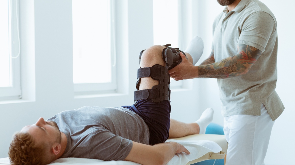 Young physiotherapist exercises in a bright medical office with his injured patient